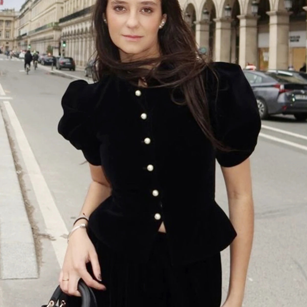 Woman wearing a black peplum top with white buttons on a city street. Velvet Puff sleeve posh classy top