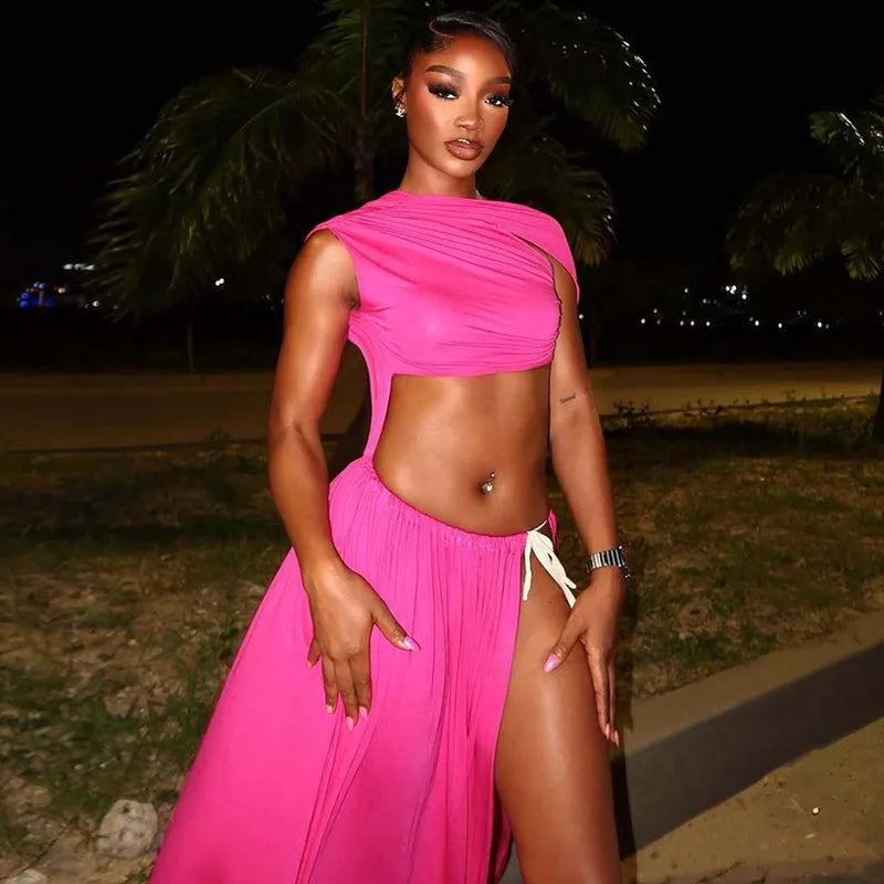 Woman in a pink outfit standing outdoors at night with palm trees in the background.