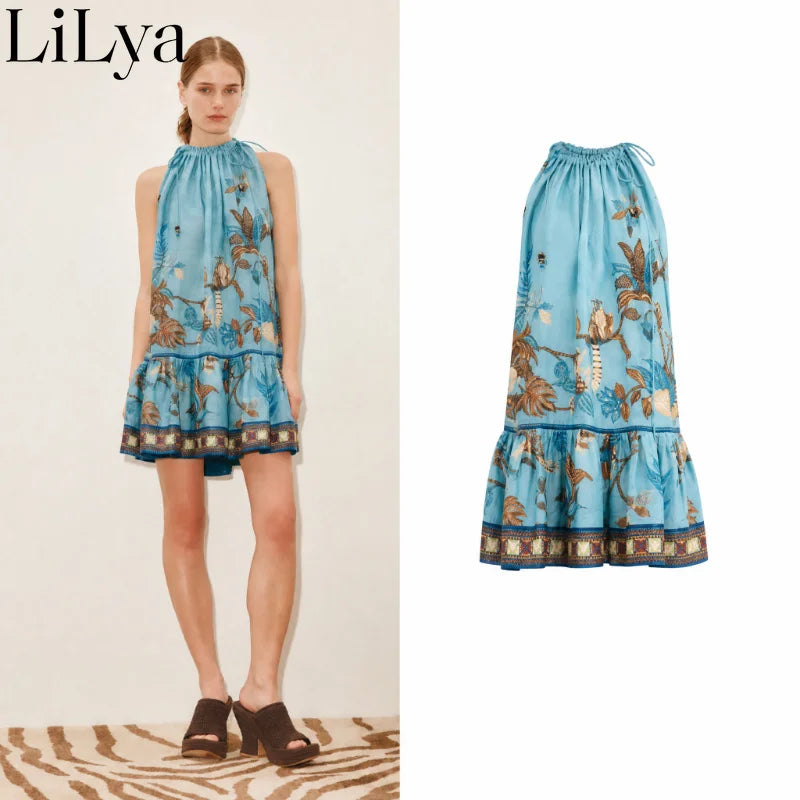 A model wears a sleeveless halter-neck tiered dress in light blue with a brown and beige botanical print, shown in a split view against a beige wall on the left and a white studio background on the right. The brand name 'LiLya' is visible in the top left corner.